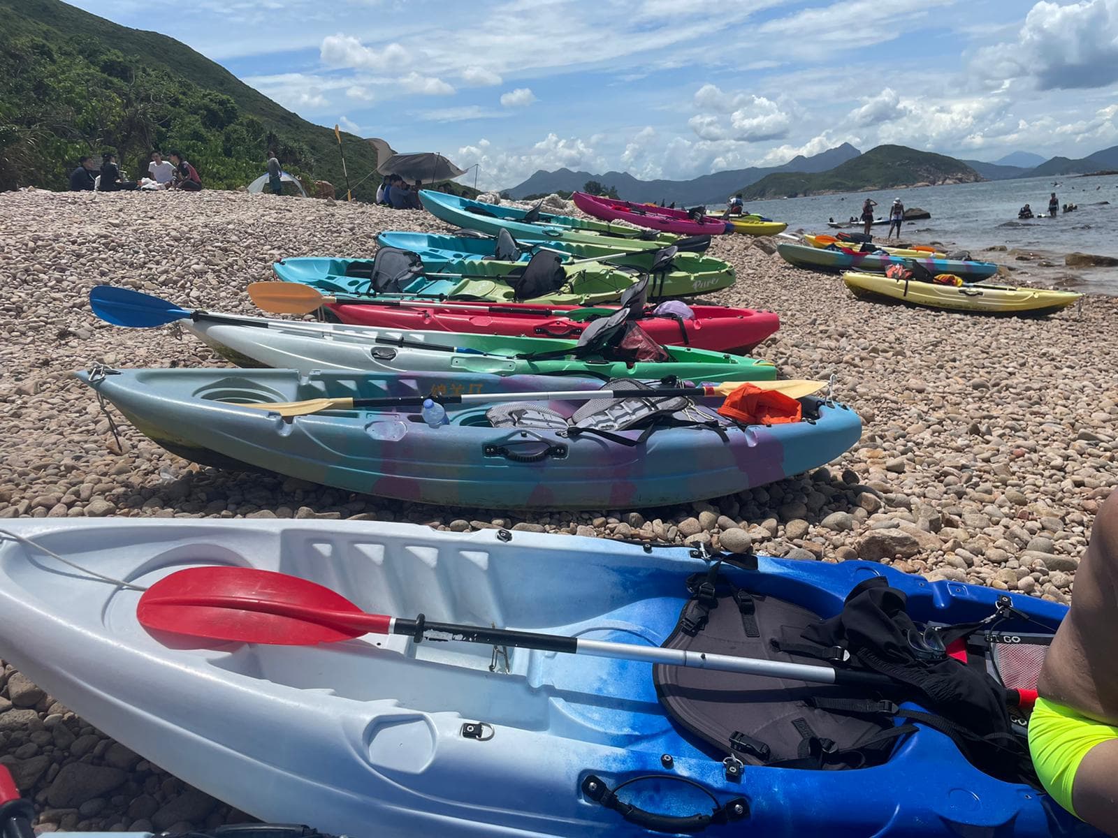 鹅卵石海滩上整齐排列着五颜六色的皮划艇,背景是碧海蓝天和群山。