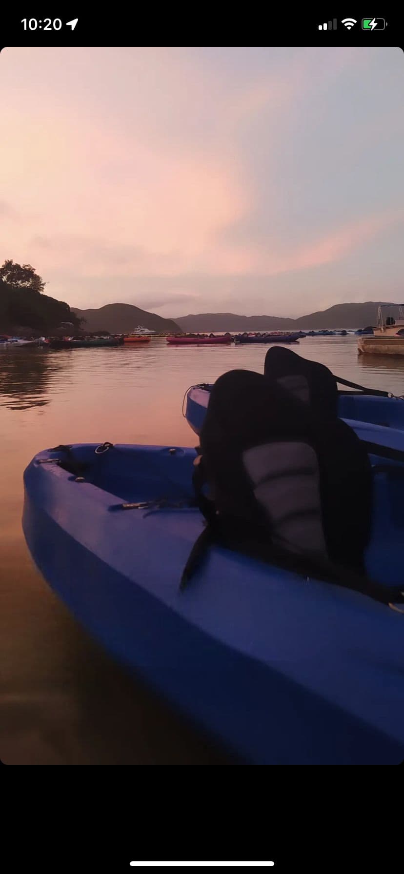 暮色下平静水面上的蓝色皮划艇,背景是粉色天空与远山。